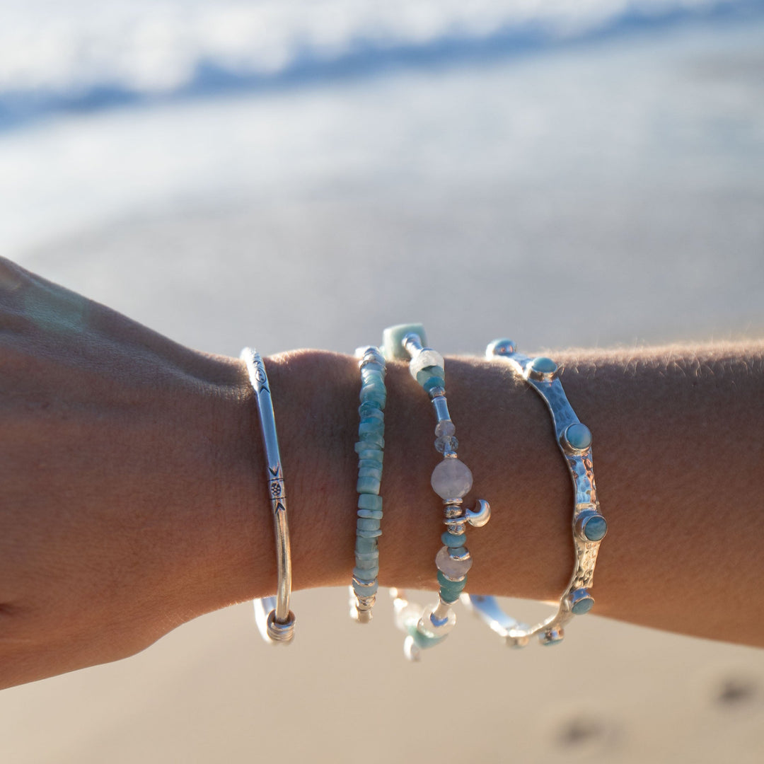 Close-up of a wrist wearing multiple beaded bracelets with a blurred beach background